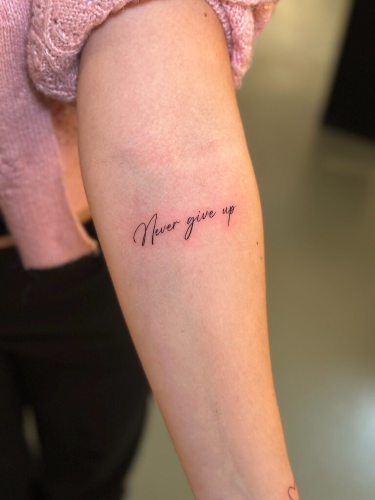 Never give up als Fineline Tattoo auf dem Unterarm
